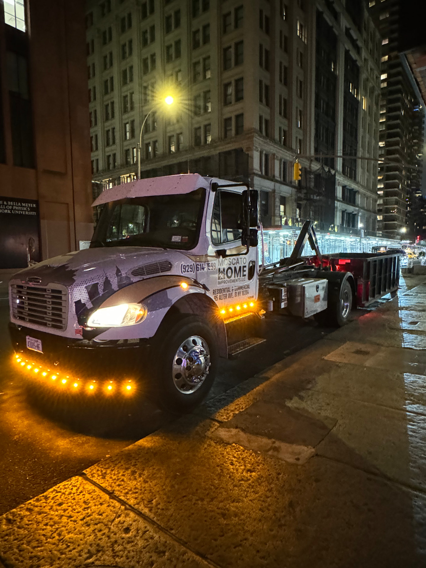 Moscato roll-off truck parked on a Staten Island street at night with bright amber underglow lighting